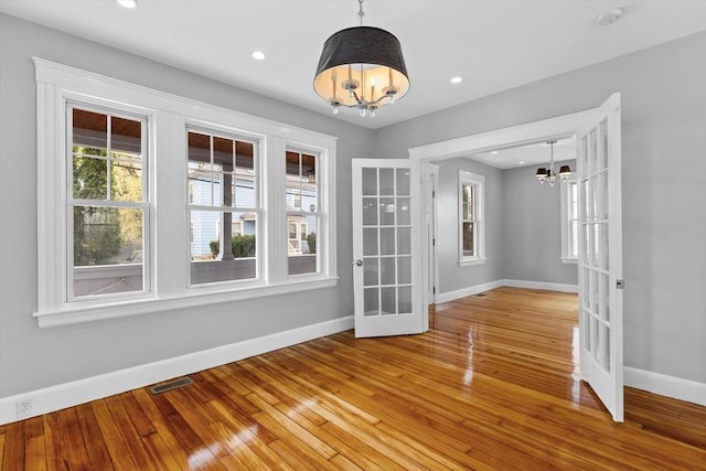 empty room featuring french doors, visible vents, baseboards, an inviting chandelier, and light wood-style flooring