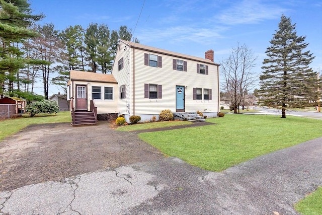 view of front of property with entry steps, a front yard, and a chimney