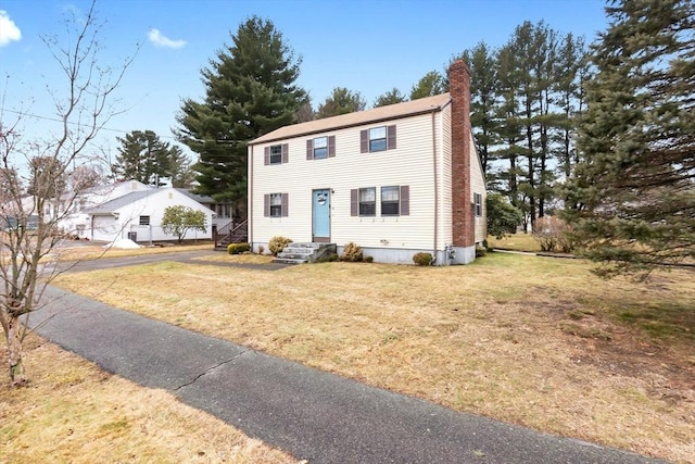 colonial home featuring a chimney, a front lawn, and entry steps