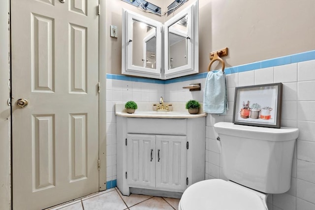 half bath featuring tile walls, a wainscoted wall, toilet, tile patterned floors, and vanity