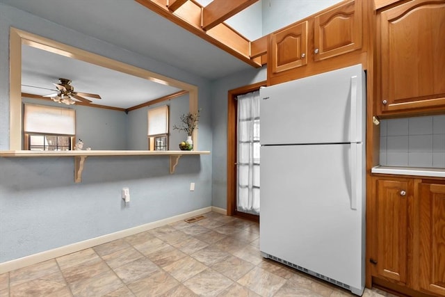 kitchen featuring baseboards, freestanding refrigerator, ceiling fan, light countertops, and brown cabinets