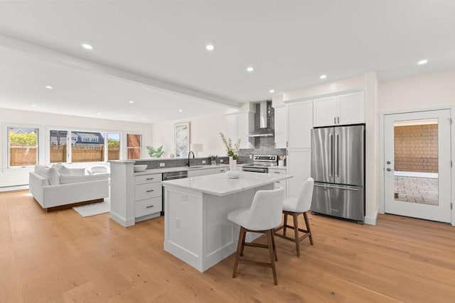 354 Gifford Unit 1, Falmouth, MA 02540 - kitchen featuring appliances with stainless steel finishes, wall chimney exhaust hood, light wood-type flooring, a kitchen island, and a breakfast bar