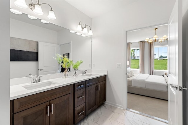 ensuite bathroom with marble finish floor, a notable chandelier, a sink, and double vanity