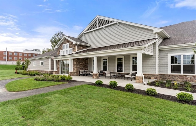 back of house featuring a lawn, stone siding, a standing seam roof, and metal roof