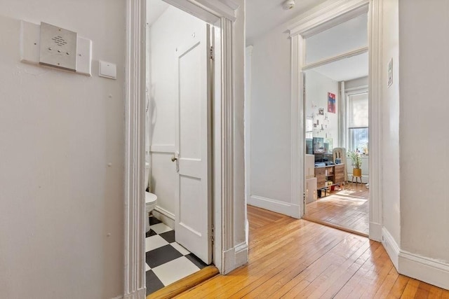 hallway with light wood finished floors, baseboards, and a desk