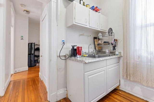 kitchen featuring a sink, light countertops, light wood-type flooring, and white cabinetry
