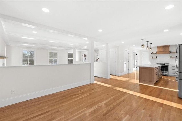 kitchen with appliances with stainless steel finishes, pendant lighting, tasteful backsplash, a center island, and light wood-type flooring