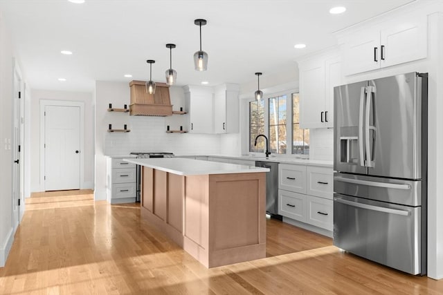 kitchen with decorative light fixtures, white cabinetry, a center island, stainless steel appliances, and light wood-type flooring