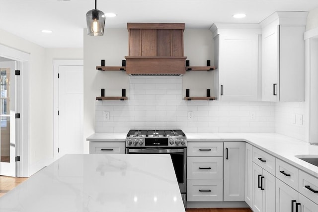 kitchen with decorative light fixtures, white cabinetry, custom exhaust hood, light stone counters, and stainless steel gas range