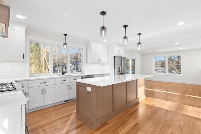 kitchen featuring a kitchen island, appliances with stainless steel finishes, pendant lighting, sink, and white cabinets