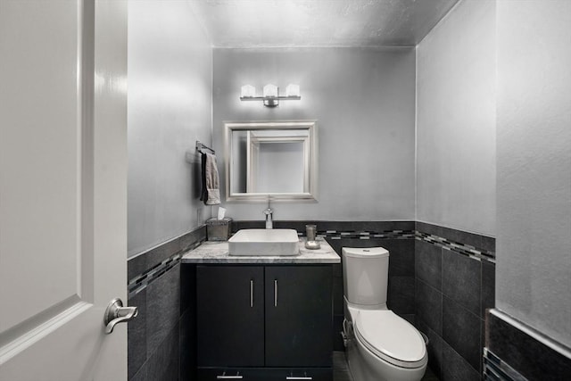 half bath with vanity, tile walls, wainscoting, and toilet