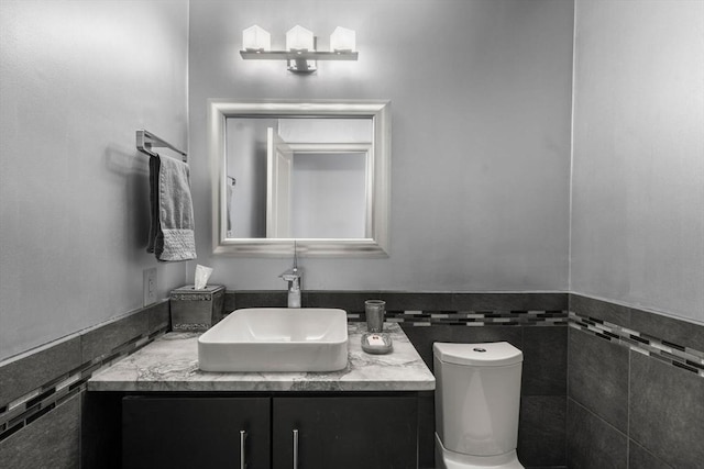 bathroom featuring vanity, a wainscoted wall, toilet, and tile walls