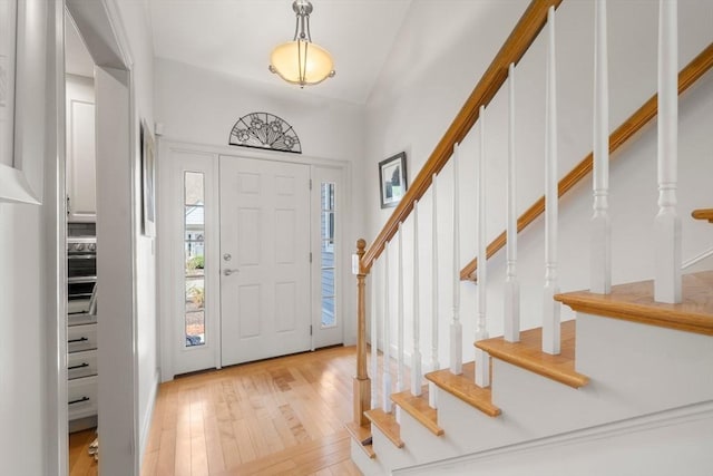 entrance foyer with light wood finished floors, stairs, and vaulted ceiling