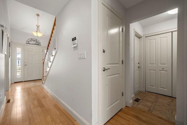 corridor with baseboards, light wood-type flooring, stairs, and visible vents