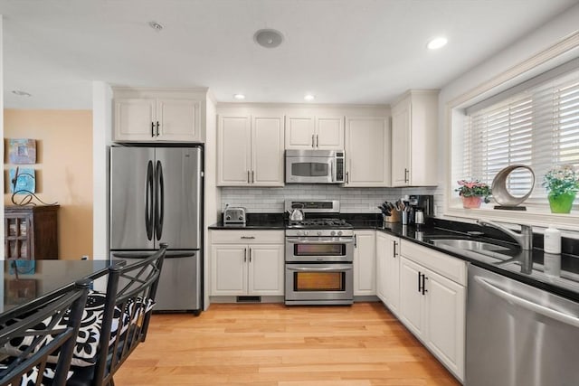 kitchen featuring dark countertops, appliances with stainless steel finishes, a sink, light wood-style flooring, and decorative backsplash
