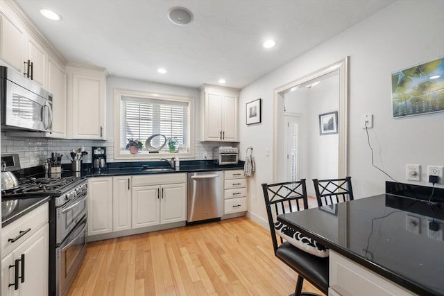 kitchen with decorative backsplash, dark countertops, light wood-style floors, white cabinetry, and appliances with stainless steel finishes