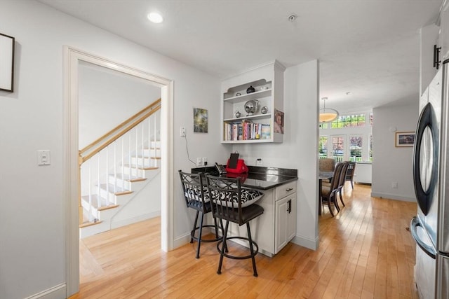 kitchen featuring open shelves, dark countertops, light wood-style flooring, freestanding refrigerator, and baseboards
