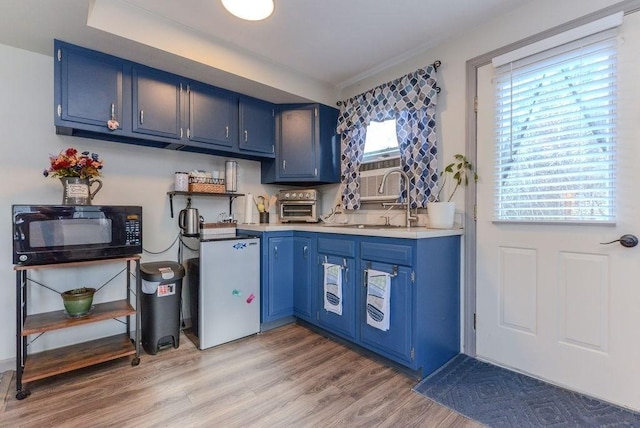 kitchen featuring blue cabinetry, stainless steel fridge, light hardwood / wood-style floors, and sink