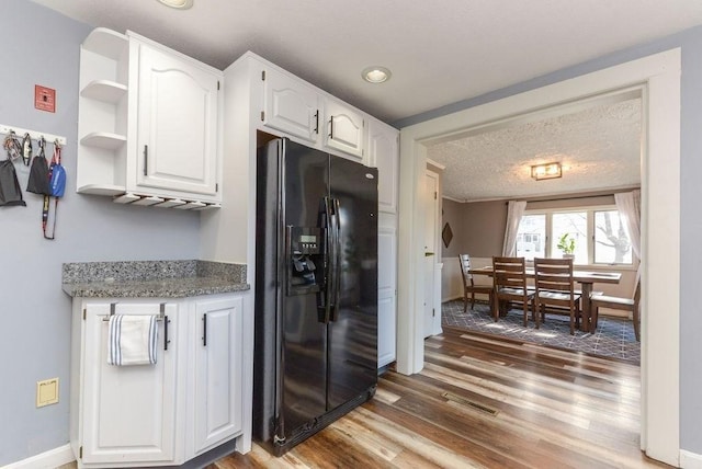 kitchen with white cabinets, a textured ceiling, stone countertops, black fridge with ice dispenser, and wood-type flooring