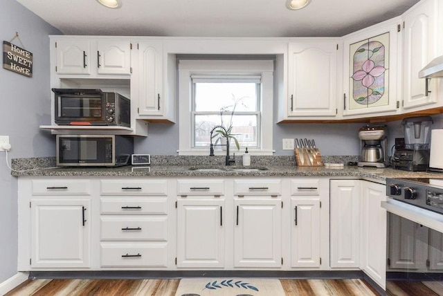 kitchen featuring white cabinets, range, dark stone countertops, and sink