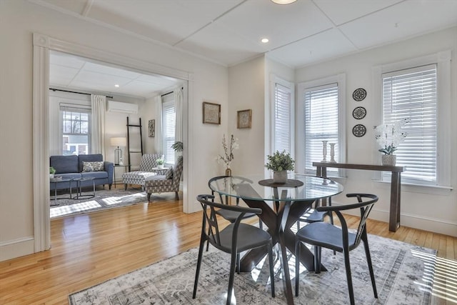 dining space with light wood-style floors, a wall unit AC, and baseboards