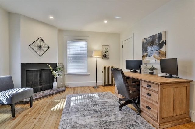 office space featuring light wood finished floors, baseboards, a fireplace with raised hearth, radiator heating unit, and recessed lighting