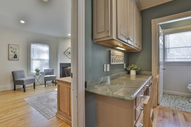 kitchen featuring a fireplace, light brown cabinets, light wood-style flooring, and baseboards