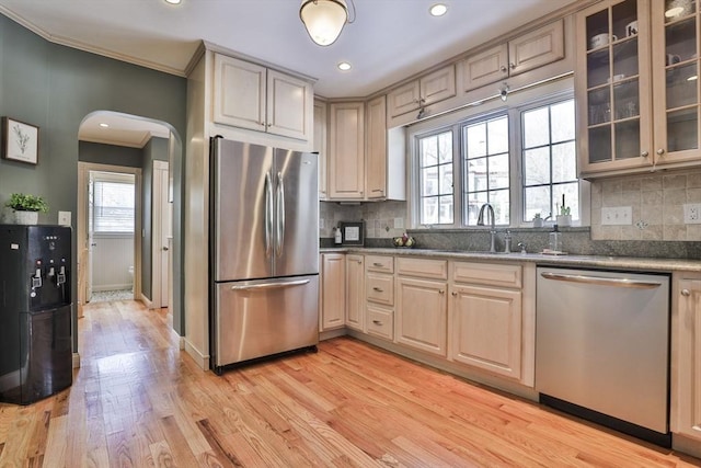 kitchen with arched walkways, stainless steel appliances, a sink, light wood-style floors, and glass insert cabinets