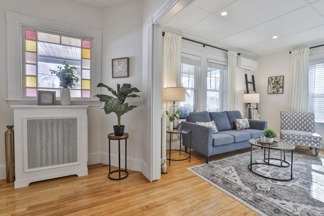 living area featuring light wood-type flooring, a wall unit AC, baseboards, and recessed lighting