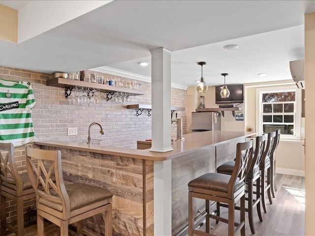 bar featuring sink, ornate columns, hardwood / wood-style flooring, ornamental molding, and brick wall