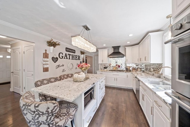 kitchen featuring pendant lighting, white cabinetry, a center island, stainless steel appliances, and wall chimney range hood