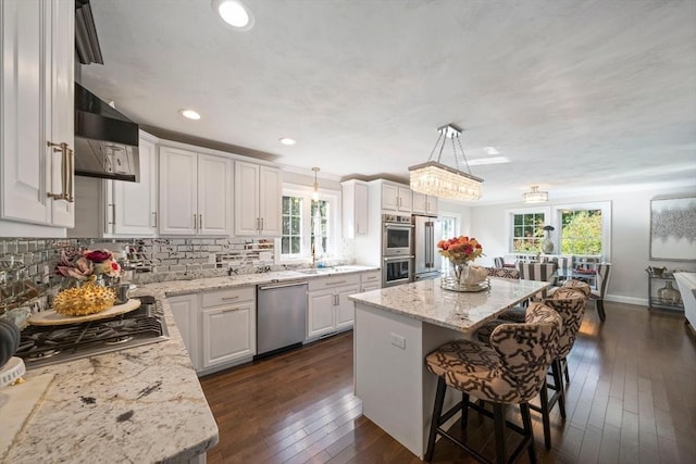 kitchen with hanging light fixtures, stainless steel appliances, a center island, light stone counters, and white cabinets