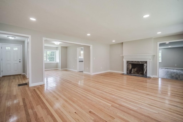 unfurnished living room with light wood finished floors, baseboards, and a high end fireplace