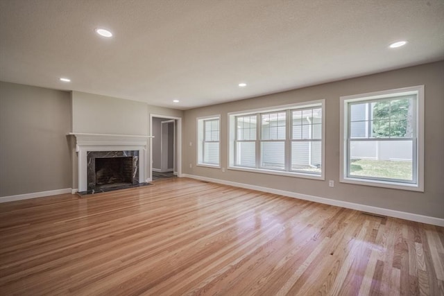 unfurnished living room with a high end fireplace, light wood-style flooring, and baseboards