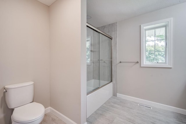 bathroom with toilet, enclosed tub / shower combo, visible vents, and baseboards