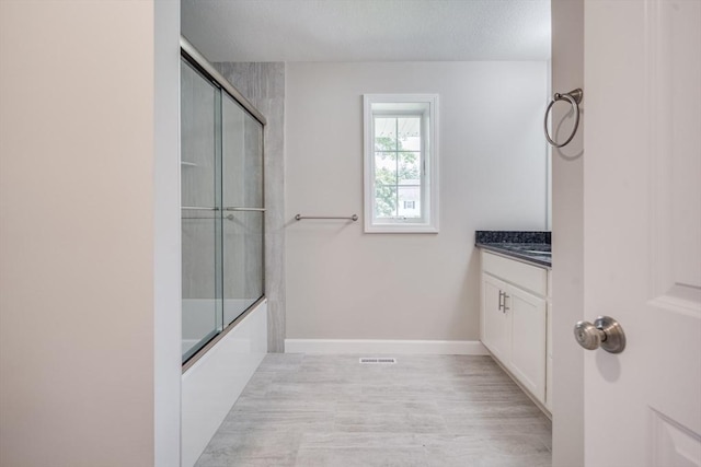 bathroom with shower / bath combination with glass door, visible vents, vanity, wood finished floors, and baseboards