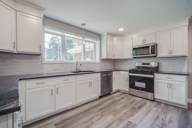 kitchen featuring light wood-style flooring, stainless steel appliances, a sink, white cabinetry, and decorative backsplash