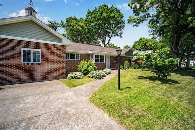 single story home featuring driveway, a front yard, and brick siding