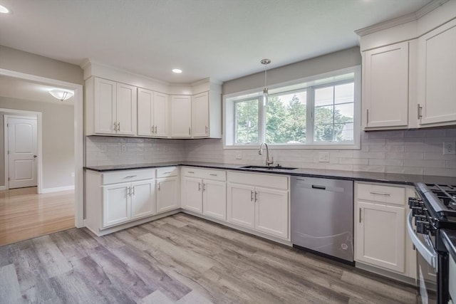 kitchen with stainless steel appliances, dark countertops, a sink, and light wood-style flooring