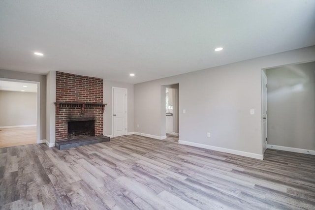 unfurnished living room featuring a brick fireplace, baseboards, wood finished floors, and recessed lighting