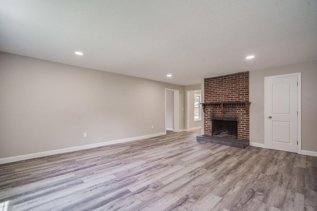 unfurnished living room featuring a brick fireplace, baseboards, wood finished floors, and recessed lighting