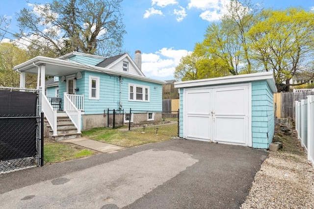 view of front of home with driveway, a chimney, fence private yard, an outdoor structure, and a storage unit