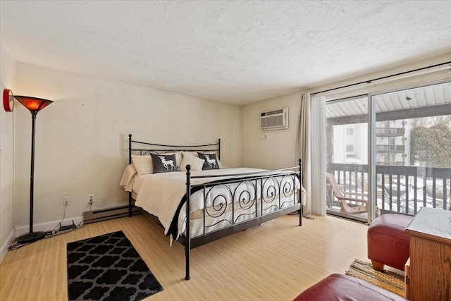 bedroom featuring light hardwood / wood-style flooring, access to exterior, a baseboard heating unit, a wall mounted AC, and a textured ceiling