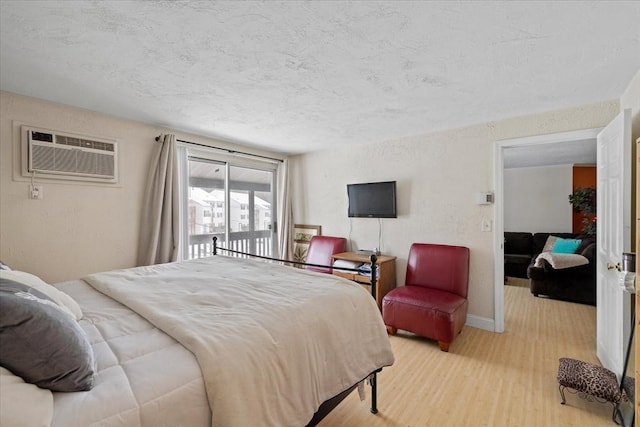 bedroom with a wall unit AC, a textured ceiling, light hardwood / wood-style flooring, and access to outside