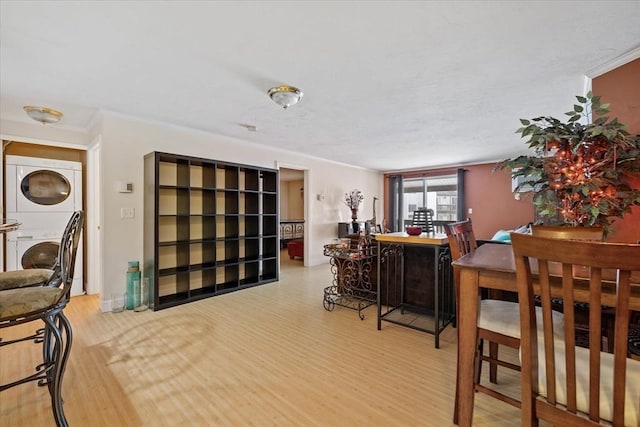 dining area with crown molding, light hardwood / wood-style flooring, and stacked washer / dryer