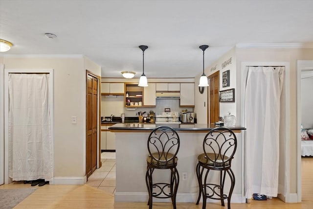 kitchen with a breakfast bar, stove, hanging light fixtures, ornamental molding, and kitchen peninsula