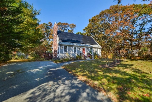 colonial inspired home featuring solar panels, a chimney, and a front lawn