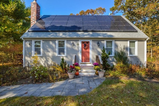 view of front of home featuring a shingled roof, solar panels, and a chimney