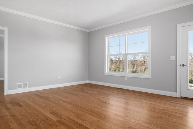 spare room with crown molding, wood finished floors, visible vents, and baseboards