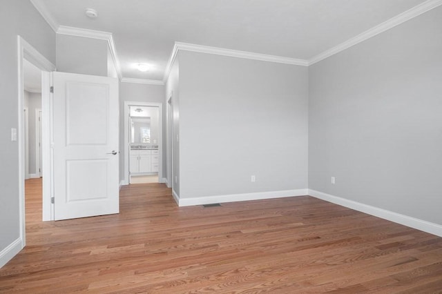 empty room with crown molding, light wood-type flooring, visible vents, and baseboards